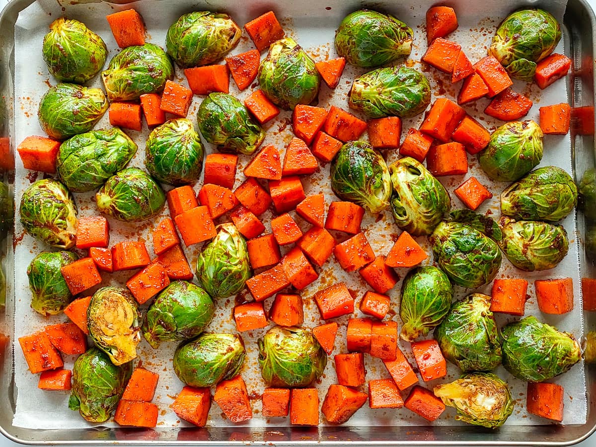 Diced and seasoned carrots and brussels sprouts spread out in a single layer on a rimmed baking sheet.