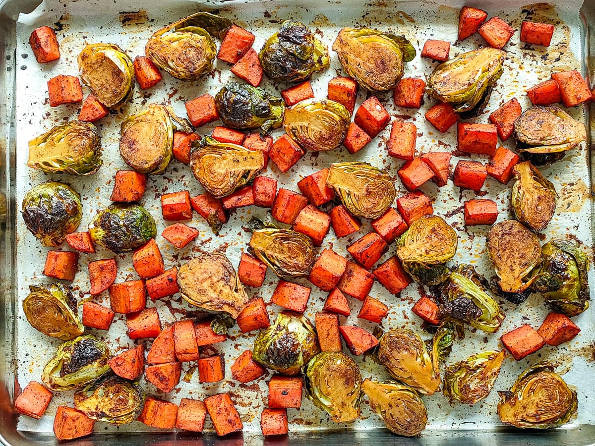 Oven roasted carrots and brussels sprouts on a rimmed baking sheet.