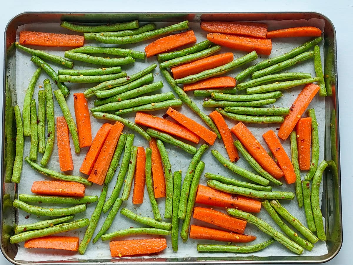 Seasoned carrots and green beans on a rimmed baking sheet.