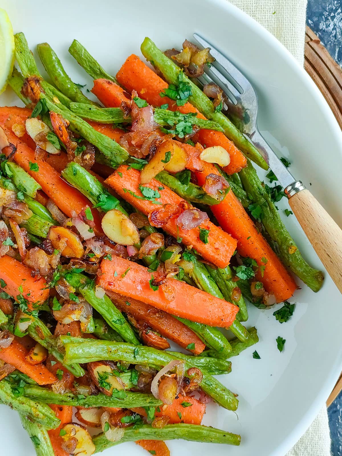 Roasted carrots and green beans with toasted almond topping and lemon wedges on a white plate.