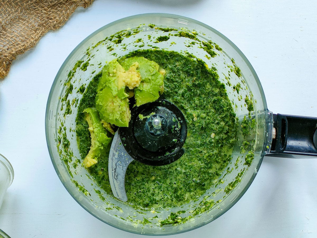 Avocado with blended herbs and spices in a food processor jar.