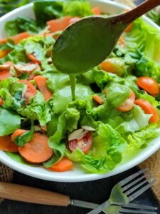 Avocado basil dressing being drizzled on spring salad on a white plate.
