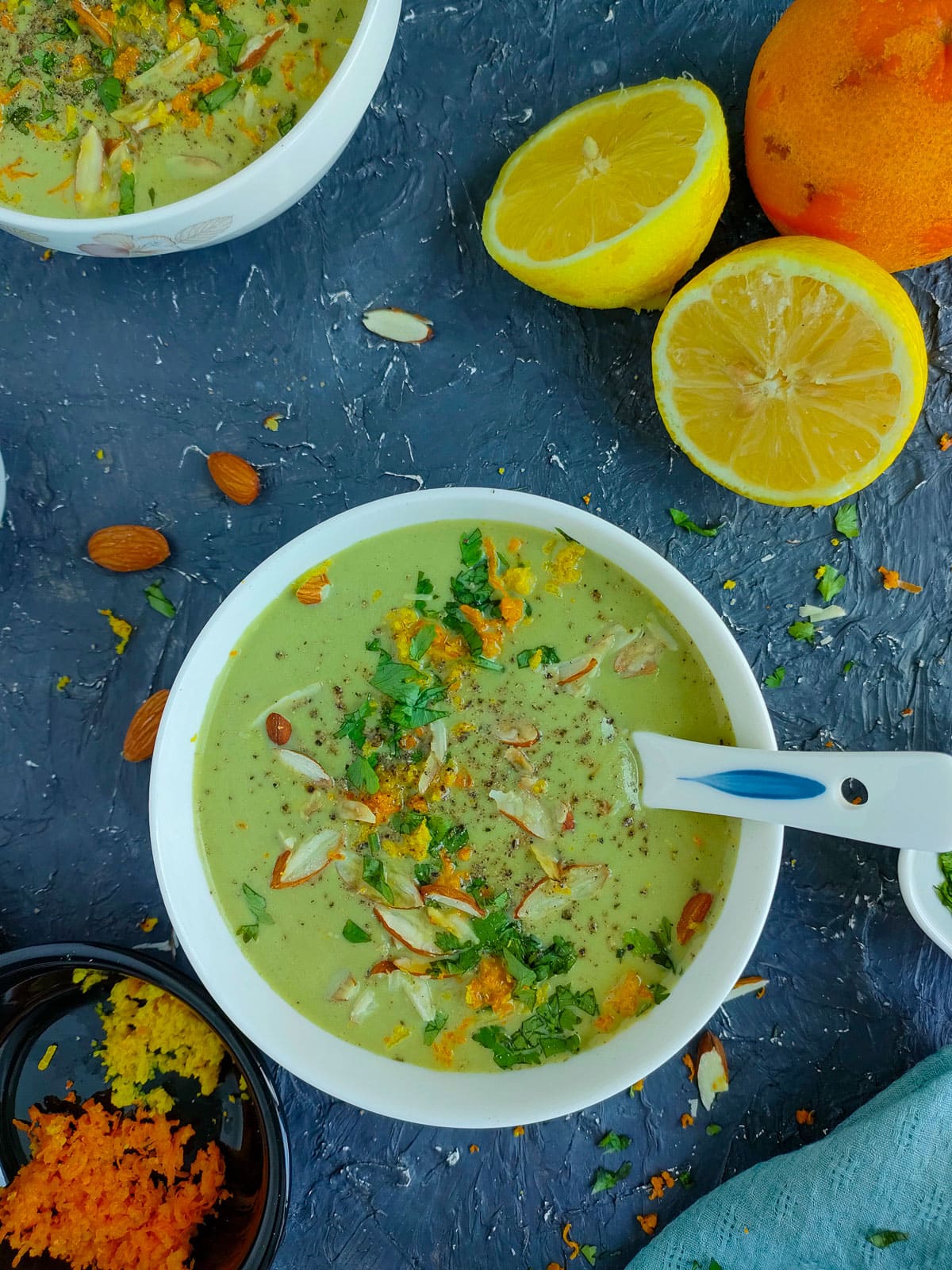 Creamy almond broccoli soup garnished with toasted almonds, parsley and lemon and orange zest in a white bowl.