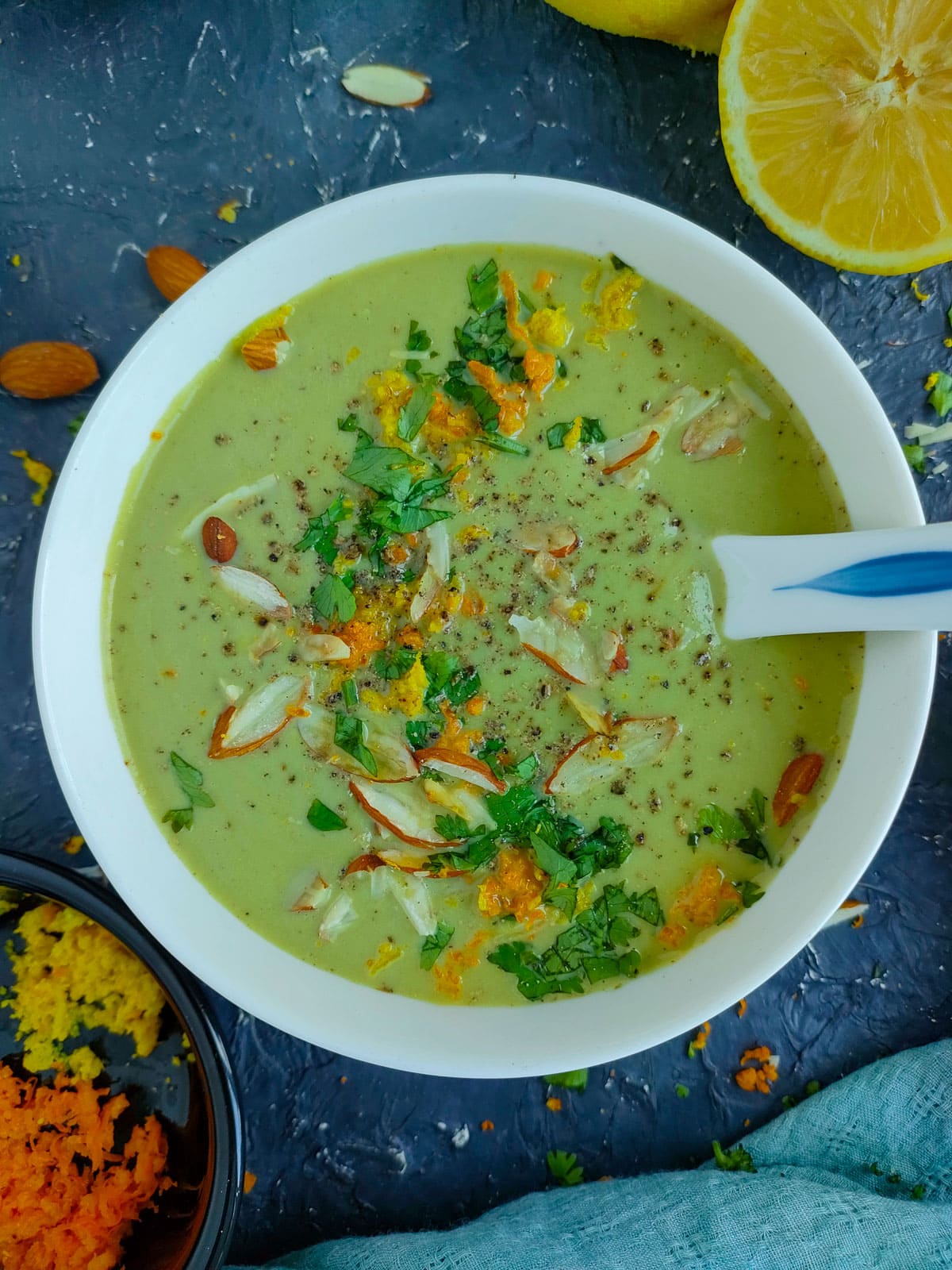 Creamy broccoli almond soup garnished with toasted almonds, parsley and lemon and orange zest in a white bowl.