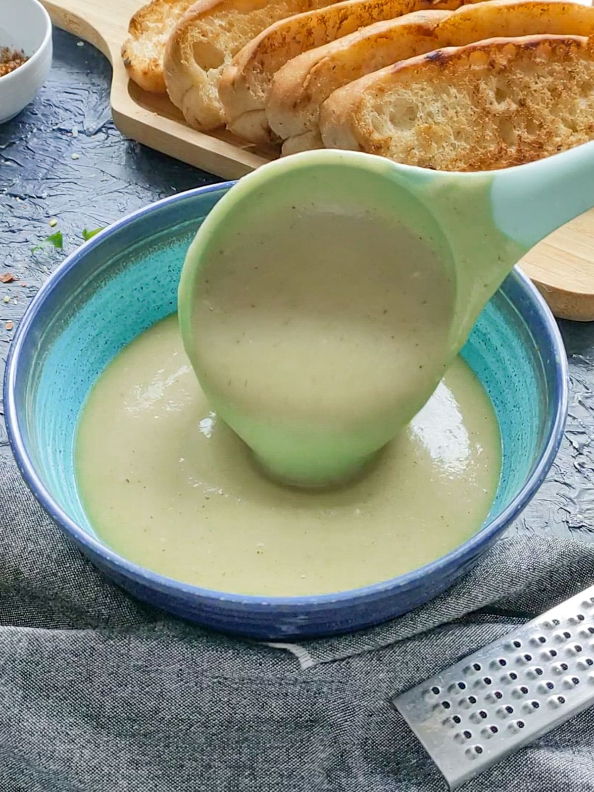 Cauliflower potato leek soup being poured into a blue bowl with a ladle.