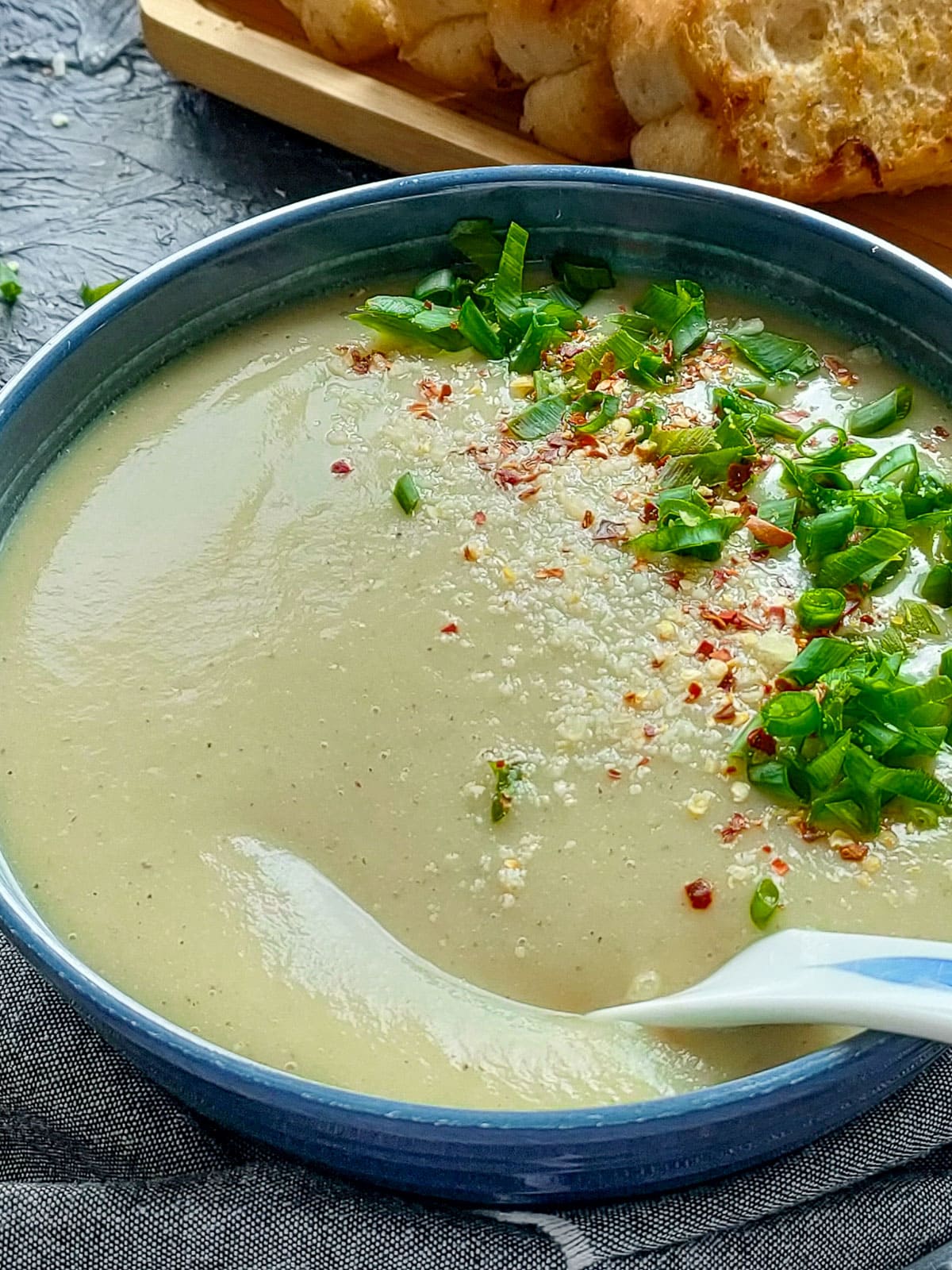 Leek potato cauliflower soup without cream in a blue bowl and a tray of crusty bread next to it.