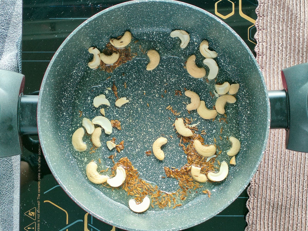 Cumin seeds and cashew nuts being fried in a pot.