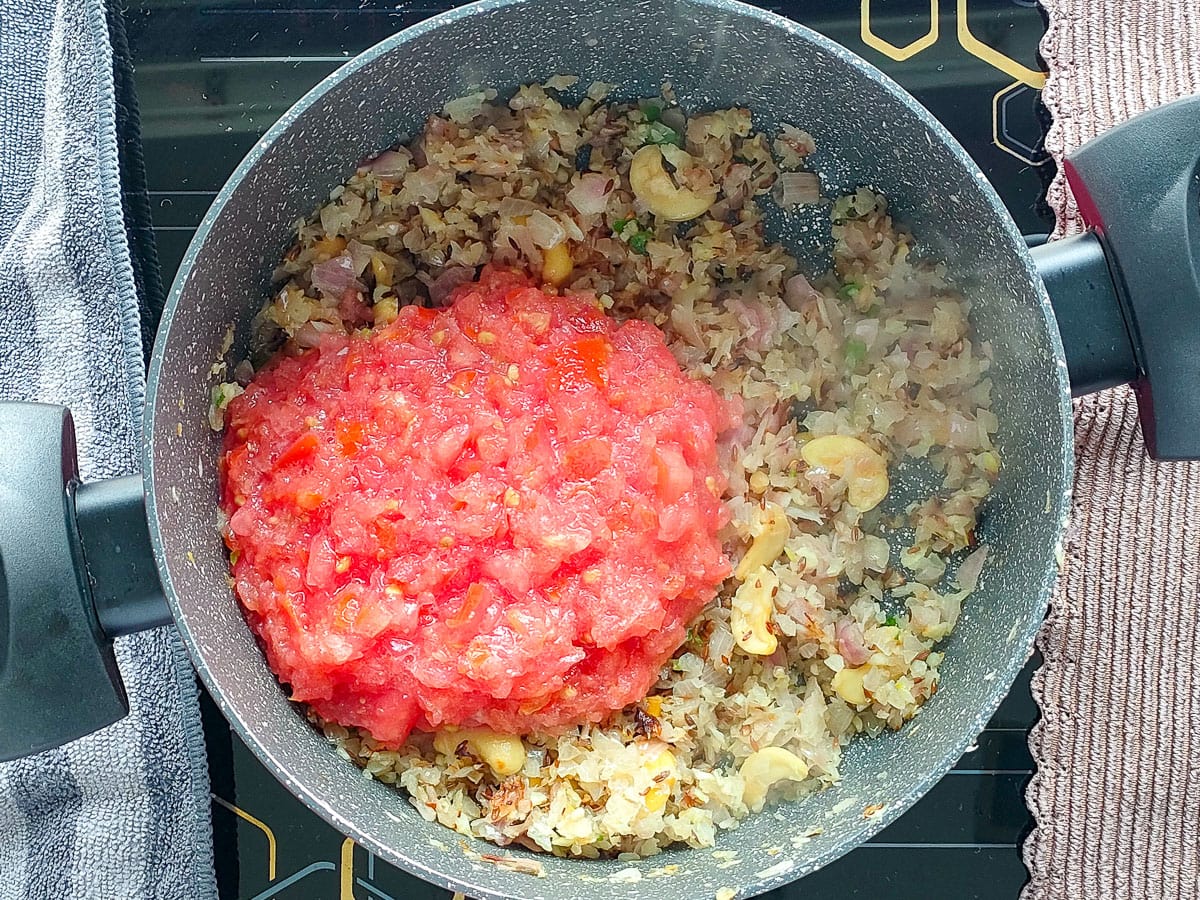 Tomatoes added to onions and other ingredients in a curry pot.