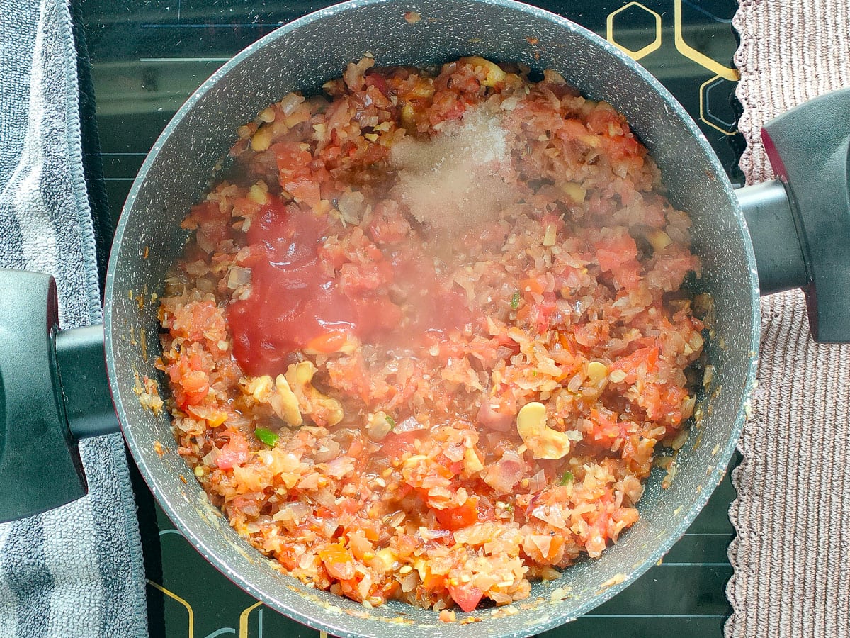 Tomato paste and salt with sauteed tomatoes and onions in a curry pot.