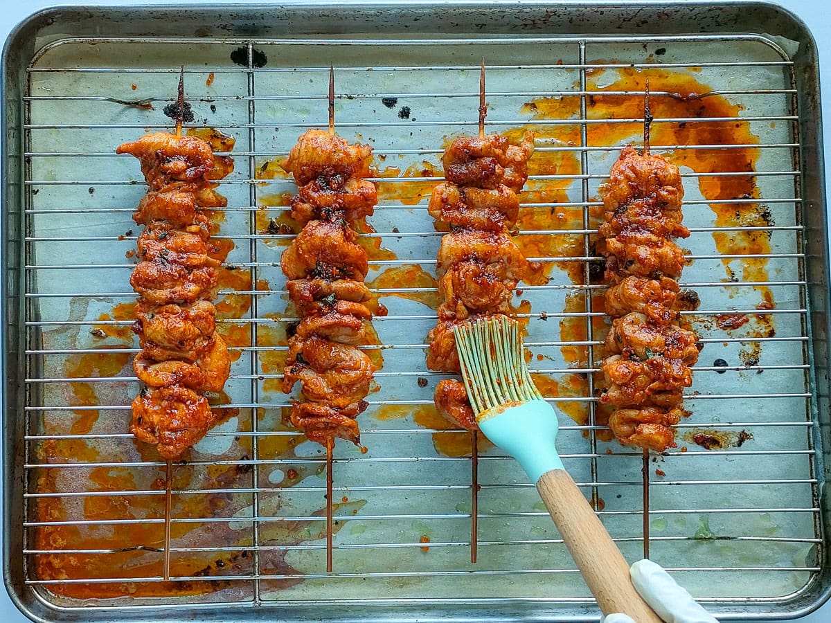 Chicken skewers being basted with butter parmesan sauce on a grilling rack.