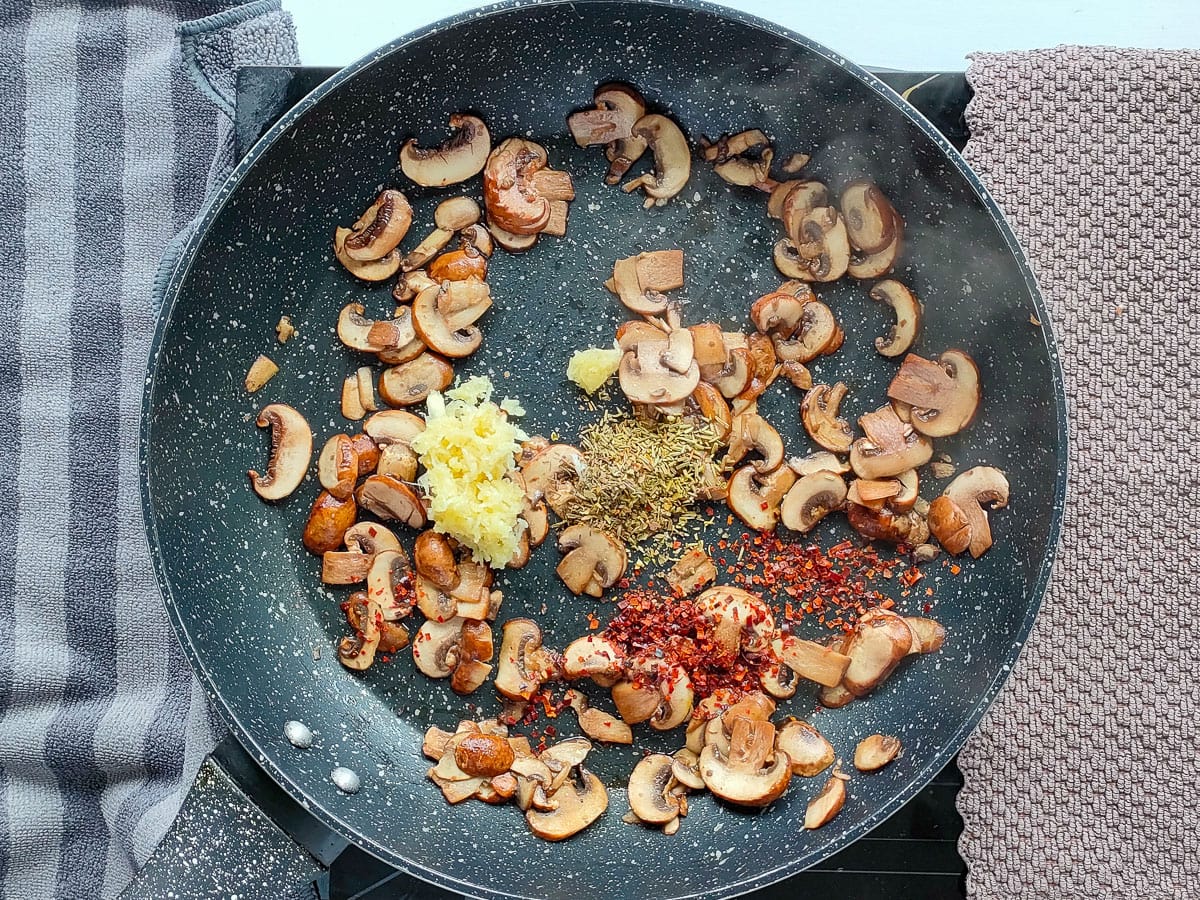 Mushrooms with garlic, red pepper flakes and dried Italian herbs in a pan.