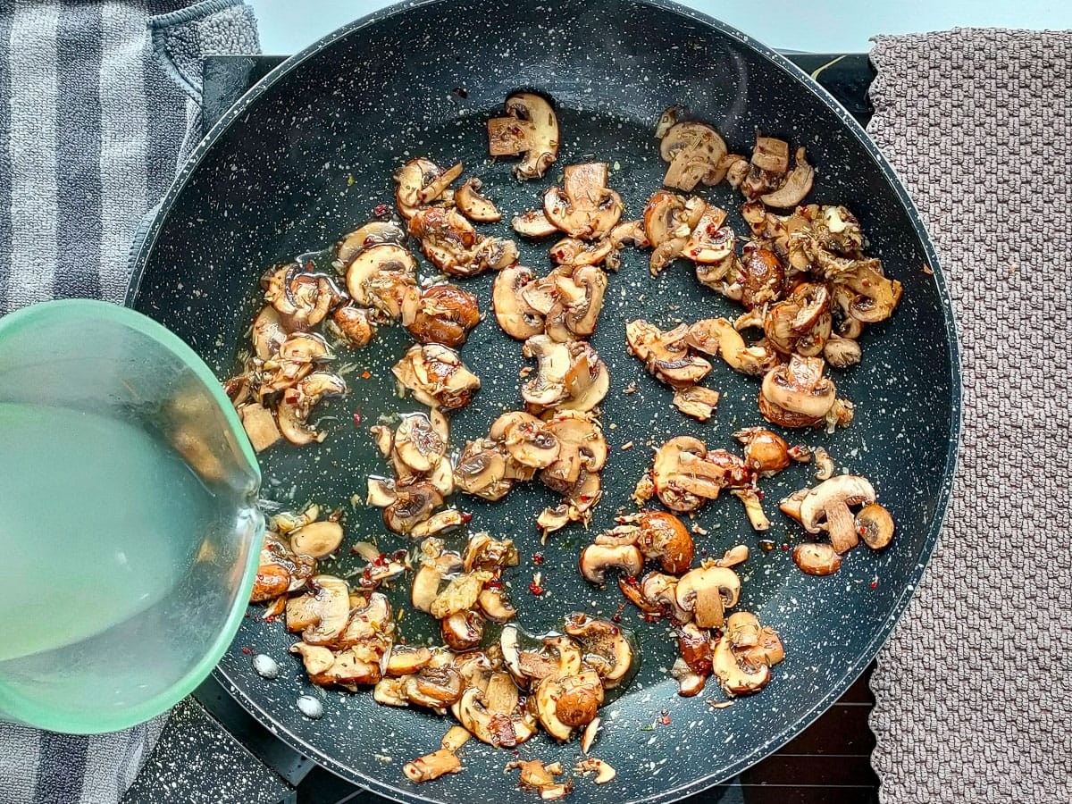 Stock being added to garlic mushrooms cooking in a pan.