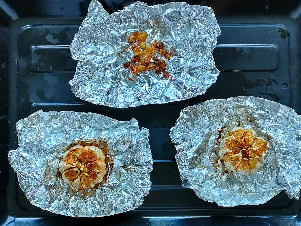 Roasted garlic bulbs on aluminum foil on a sheet pan.