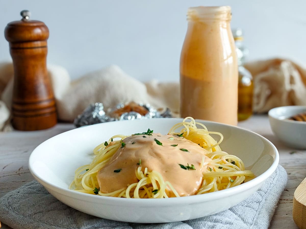 Roasted garlic sauce with pasta in a white plate and the sauce in a bottle in the background.