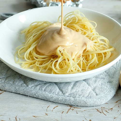 Roasted garlic pasta sauce being drizzled on pasta in a white plate.