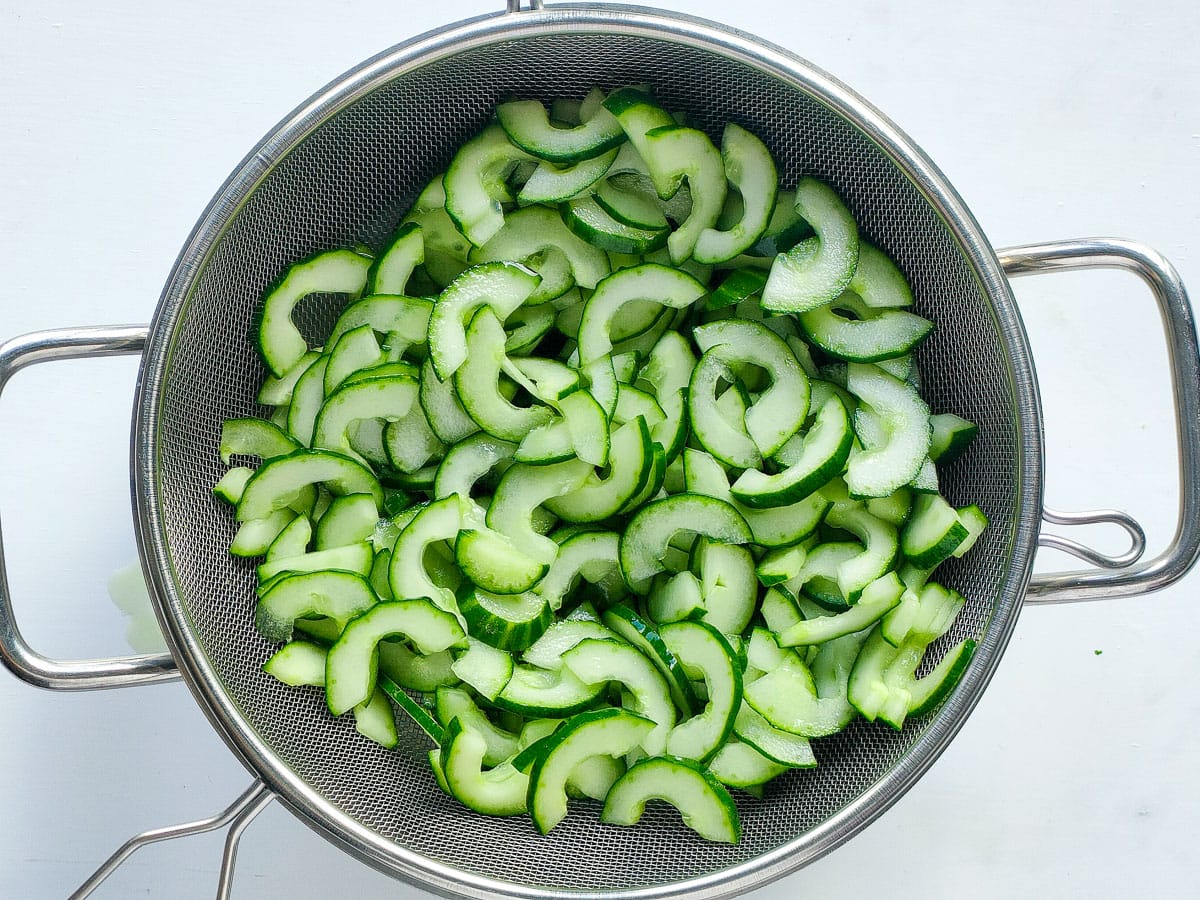 Salted cucumber slices in a colander.