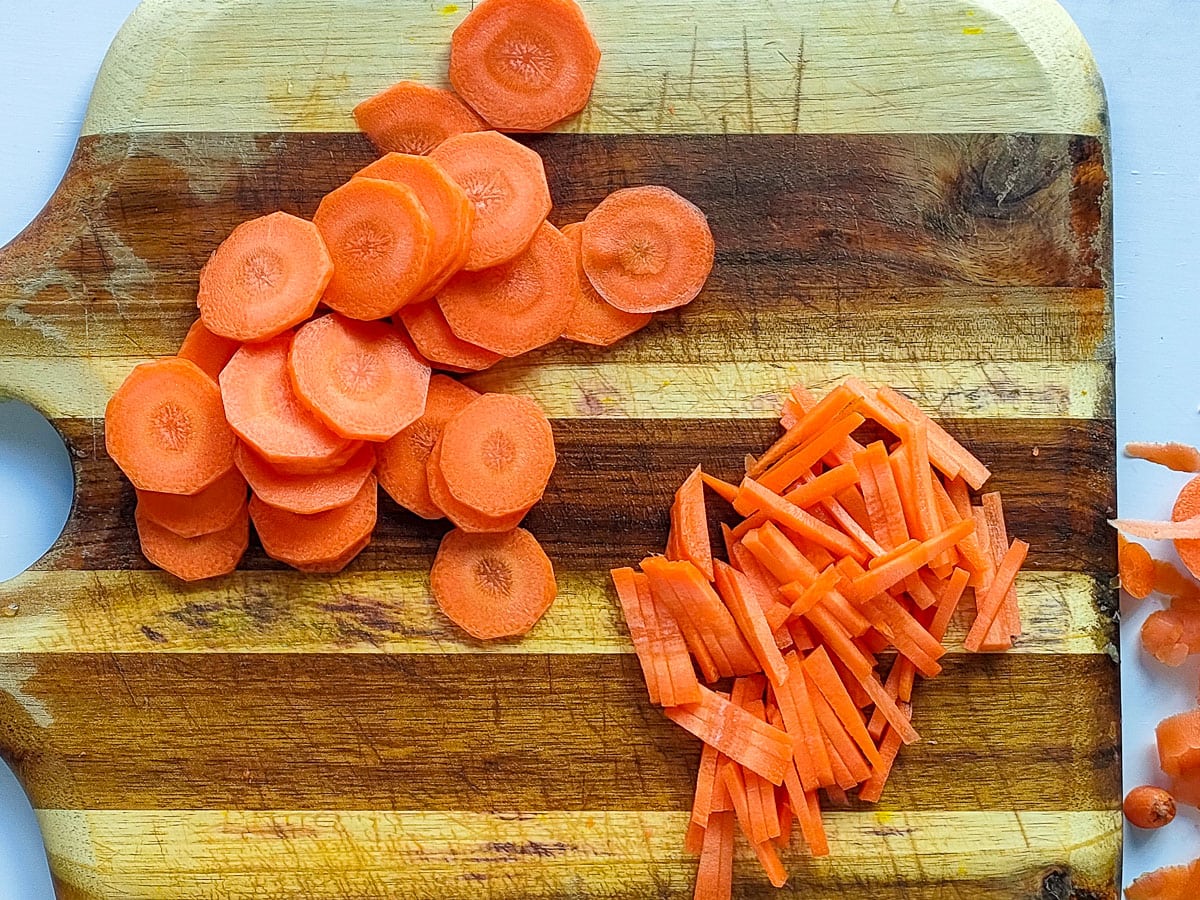 Carrots cut into discs and matchsticks on a chopping board.