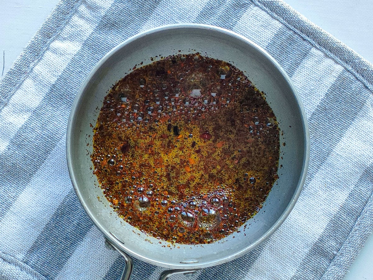 Red pepper flakes sizzling in hot sesame oil in a small pan.