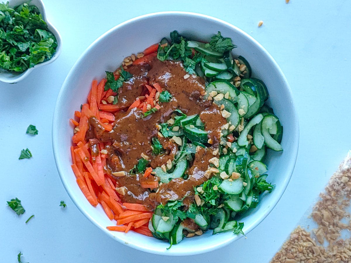 Cucumber and carrot salad with Asian sesame dressing drizzled on top in a large white bowl.