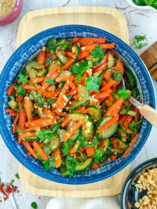 Carrot cucumber carrot salad in a blue bowl with a spoon in it.