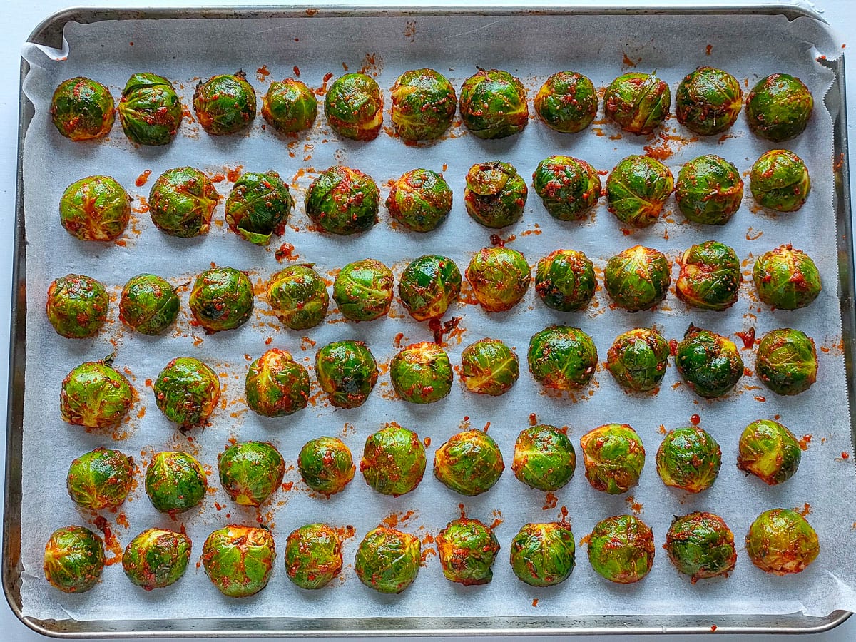 Marinated Brussel sprouts arranged in rows on a sheet pan lined with parchment paper.