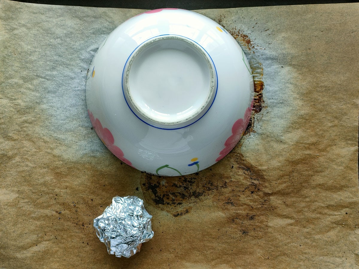 Roasted red peppers covered with a ceramic bowl and roasted garlic wrapped in foil next to it.