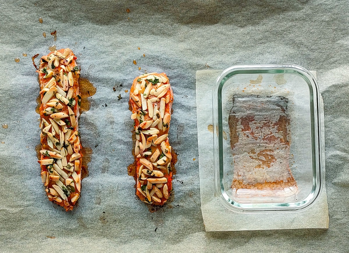 Baked salmon with almond crust and salmon skin next to it on a baking sheet.