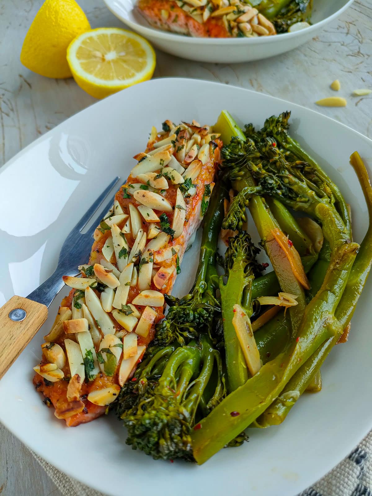 Salmon with almonds on a white plate with sauteed broccolini.