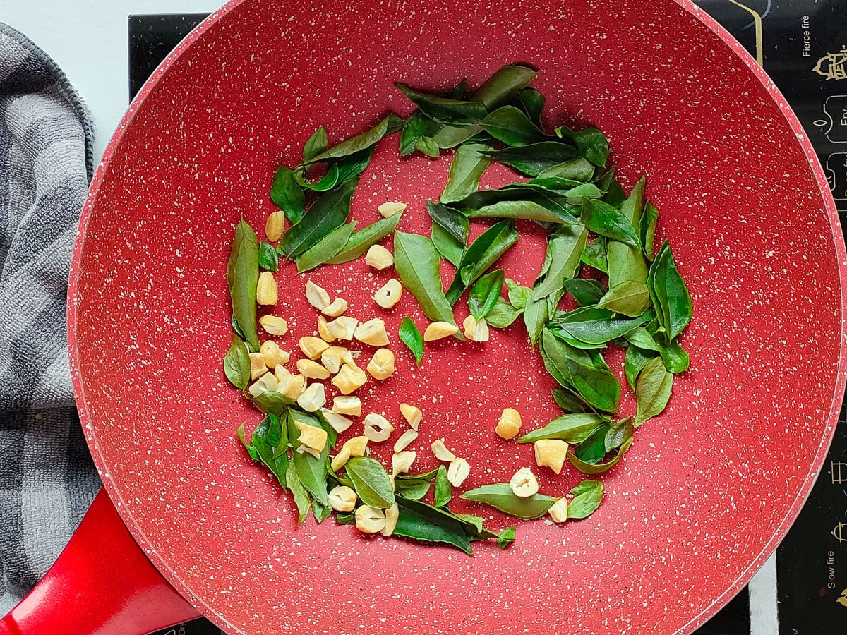 Cashews being roasted with curry leaves in a deep pan.