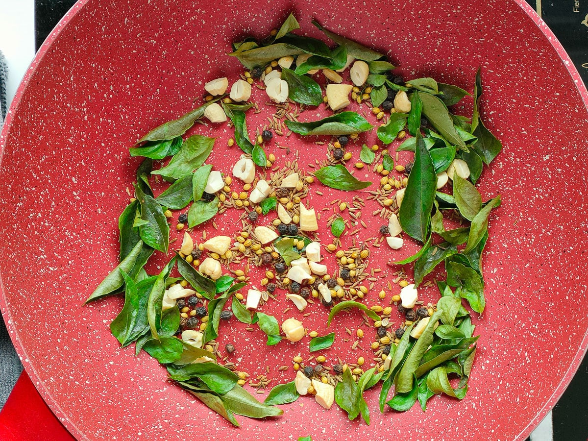 Whole spices, cashew and curry leaves being roasted in a deep pan.