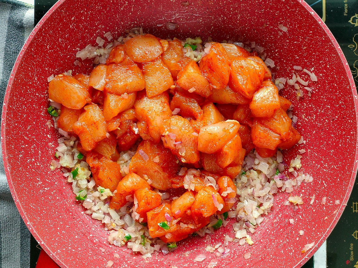 Marinated chicken cubes with sauteed onions in a deep pan.