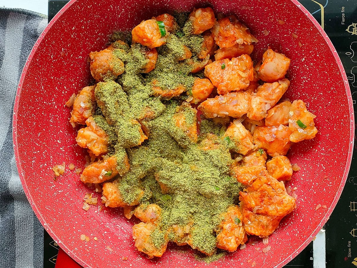 Partially cooked chicken with curry leaf-spice powder in a deep pan.
