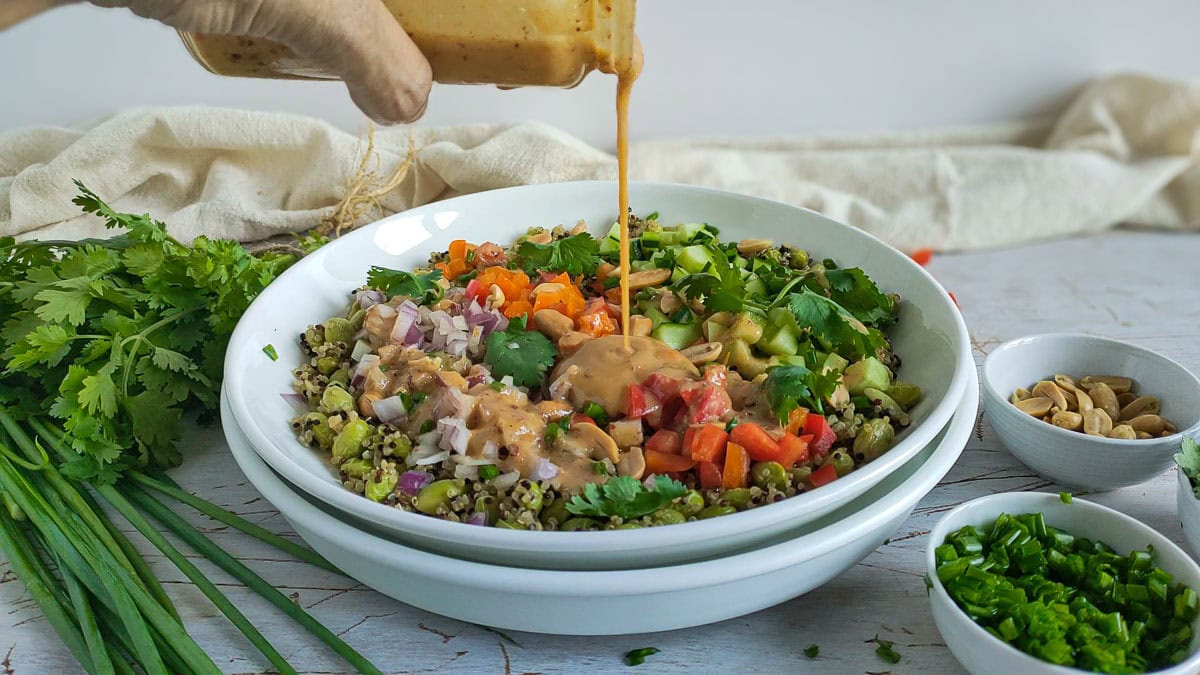 Miso salad dressing being drizzled on quinoa edamame salad on a plate.