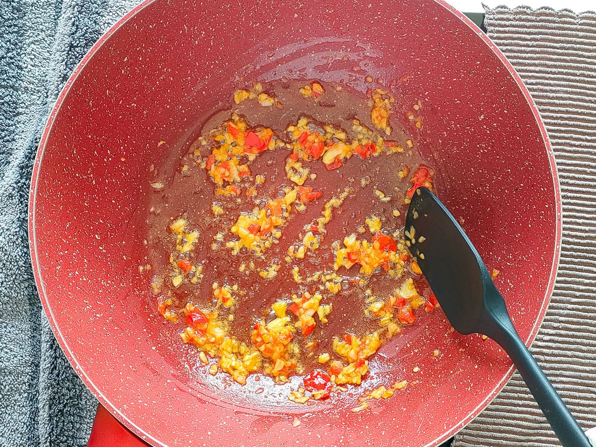 Minced garlic and chilies being stir-fried in a wok pan.