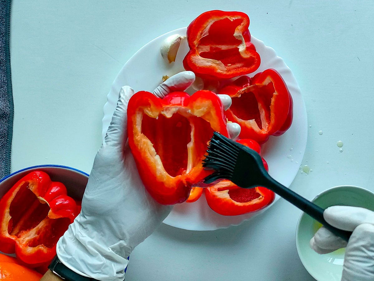 Smearing oil on halved red peppers.