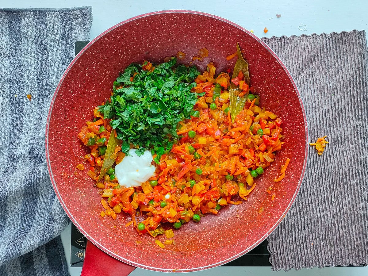 Yogurt and herbs with onion masala and veggies in a wok pan.