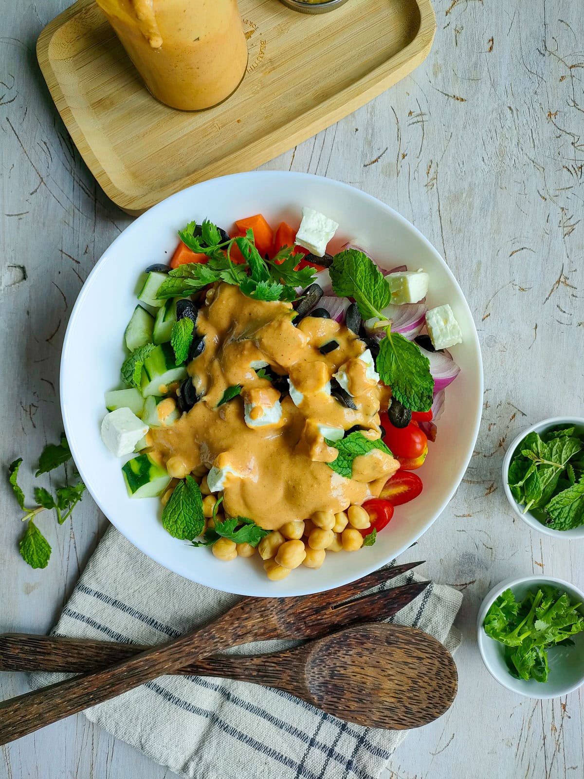 Hummus salad with dressing, fresh veggies and chickpeas in a white bowl.