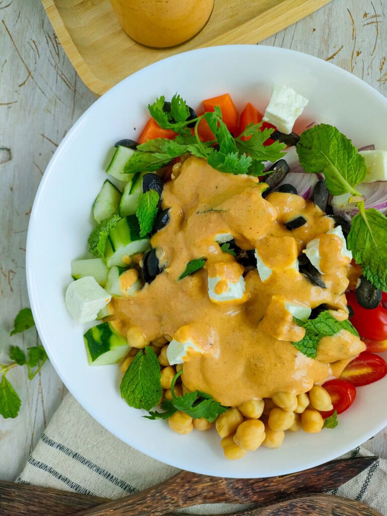 Mediterranean salad with hummus dressing in a white bowl.