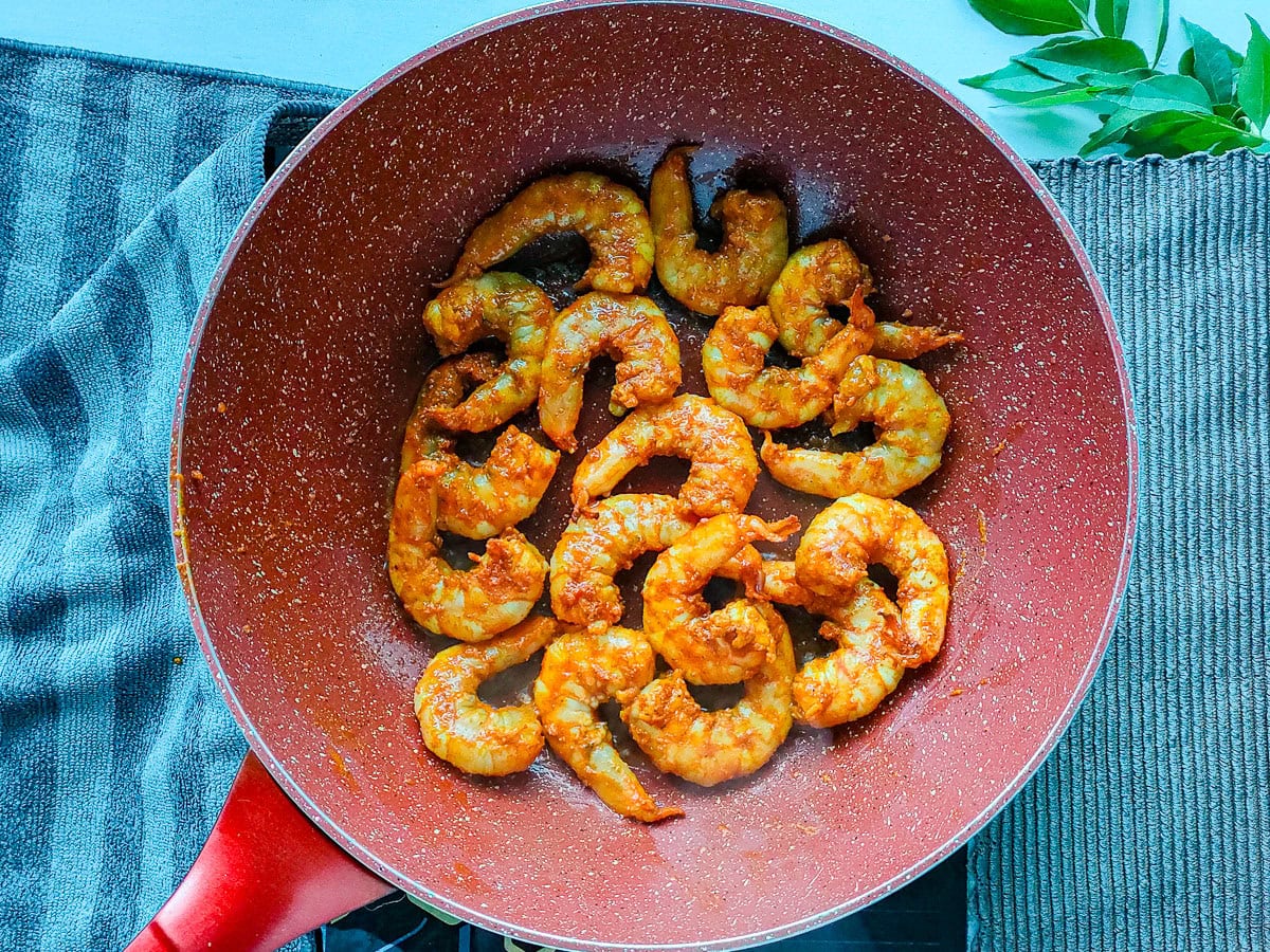 Marinated prawns being sauteed in ghee and oil in a wok pan.