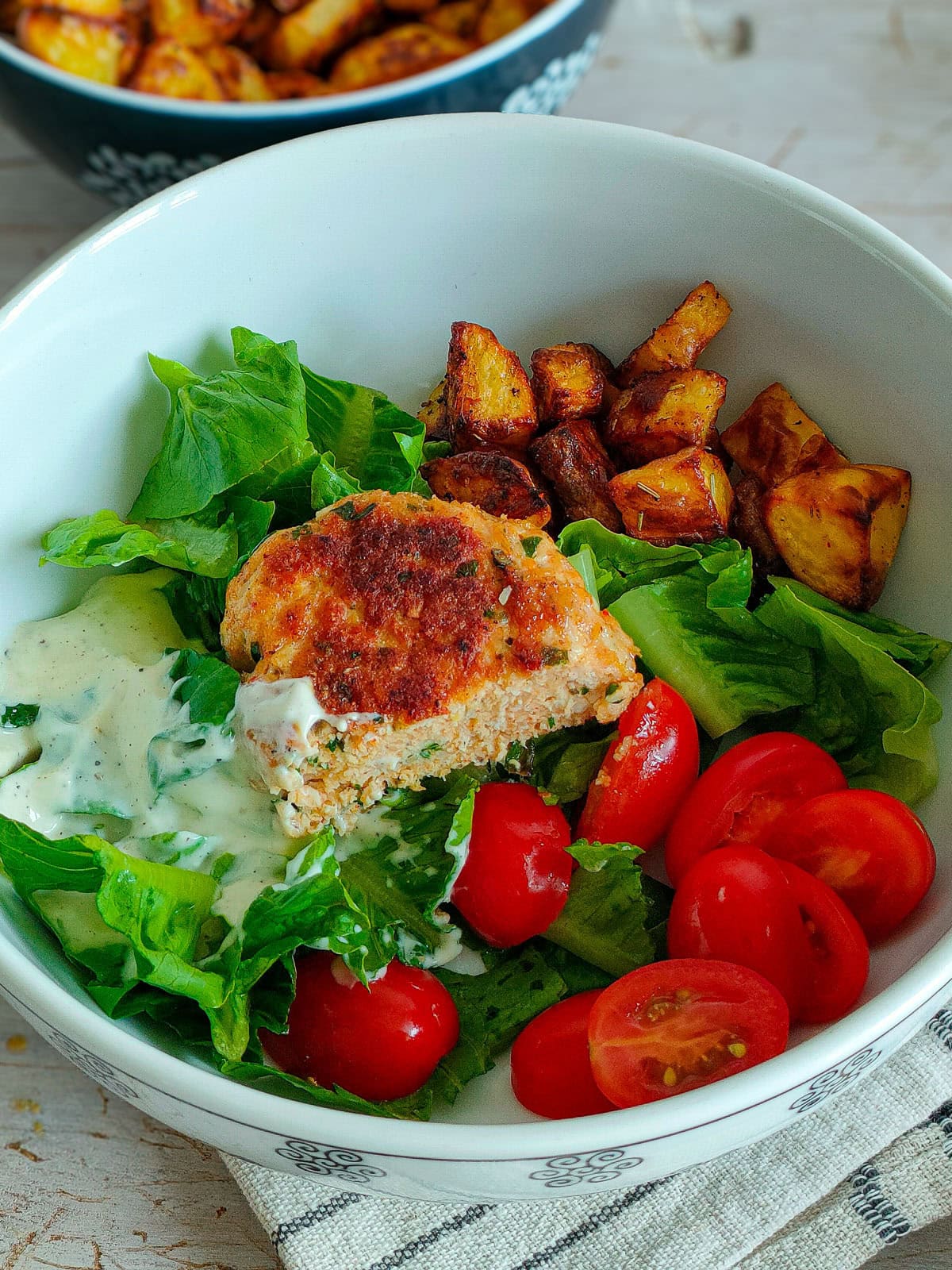 Deconstructed burger in a bowl with chicken patty, roasted potatoes and vegetables.