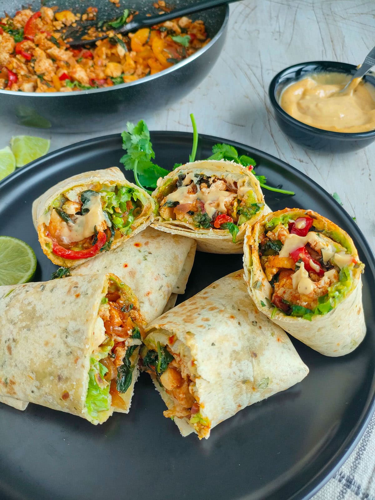 Spicy tofu wraps with roasted garlic sauce and guacamole on a black plate.