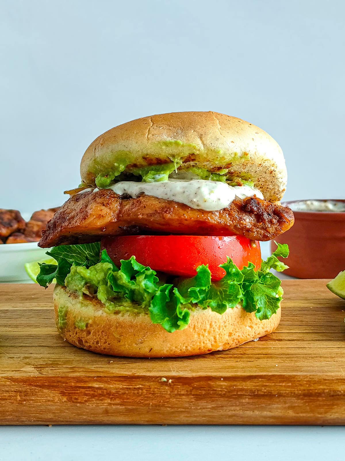 Chipotle chicken burger on a serving board with lime wedges.