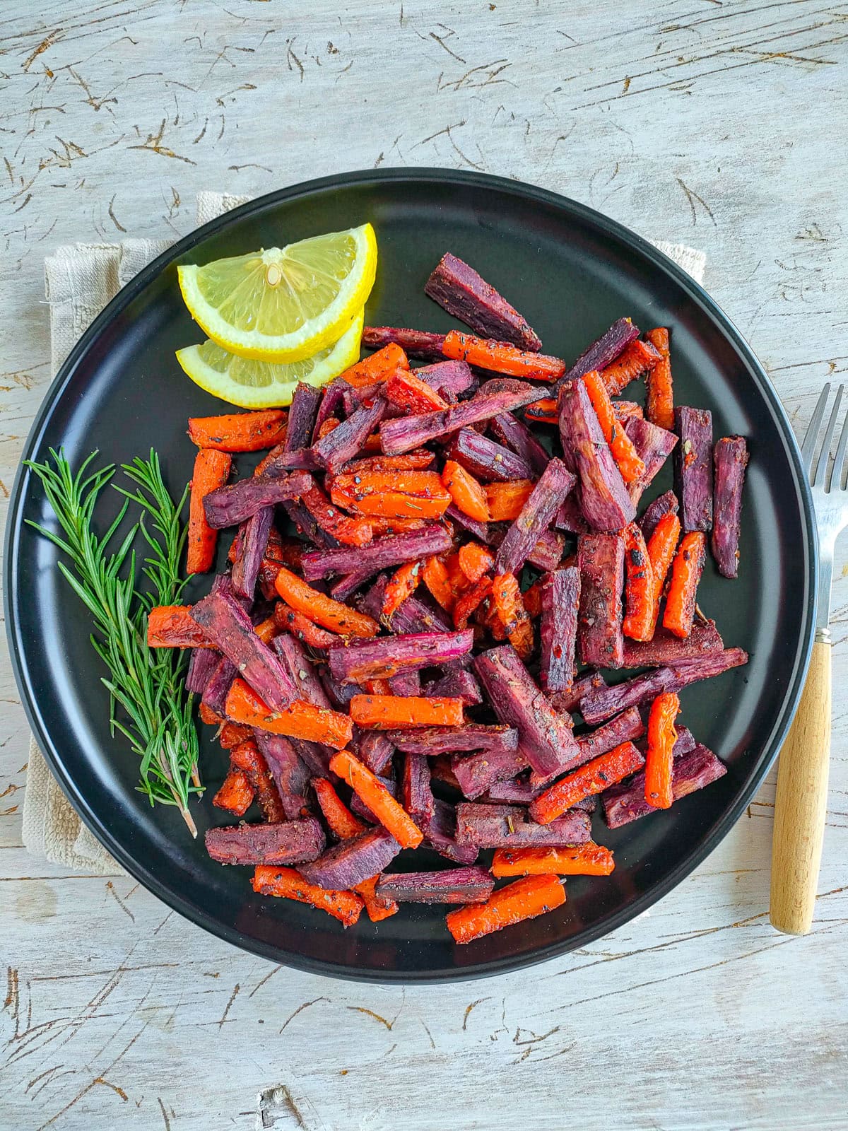 Spicy roasted carrots and sweet potatoes with lemon slices on a black plate.