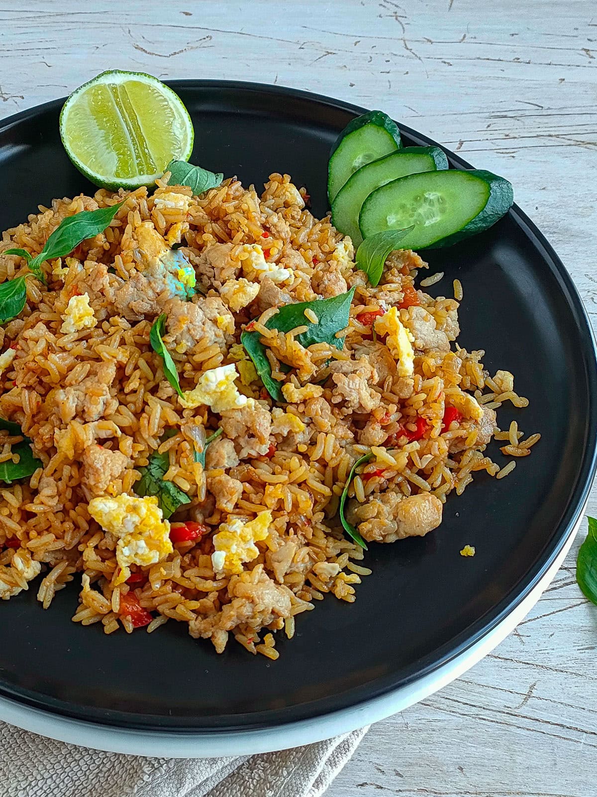Spicy basil chicken fried rice served on a black plate with cucumber slices and lime.