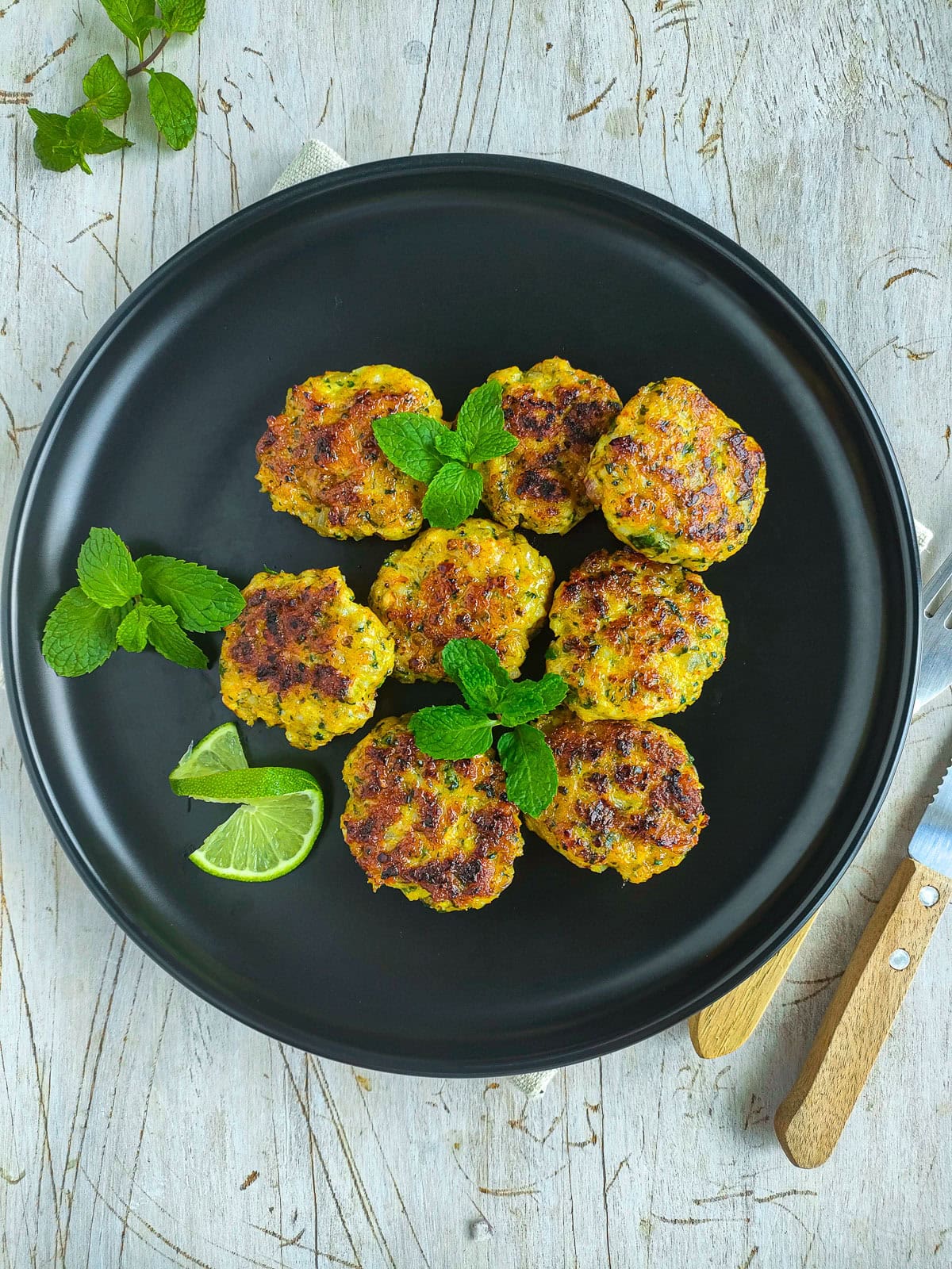 Easy Shrimp Fritters | Prawn Cutlets (no deep frying) Pan fried prawn cutlets garnished with mint leaves and a lime slice on a black plate.