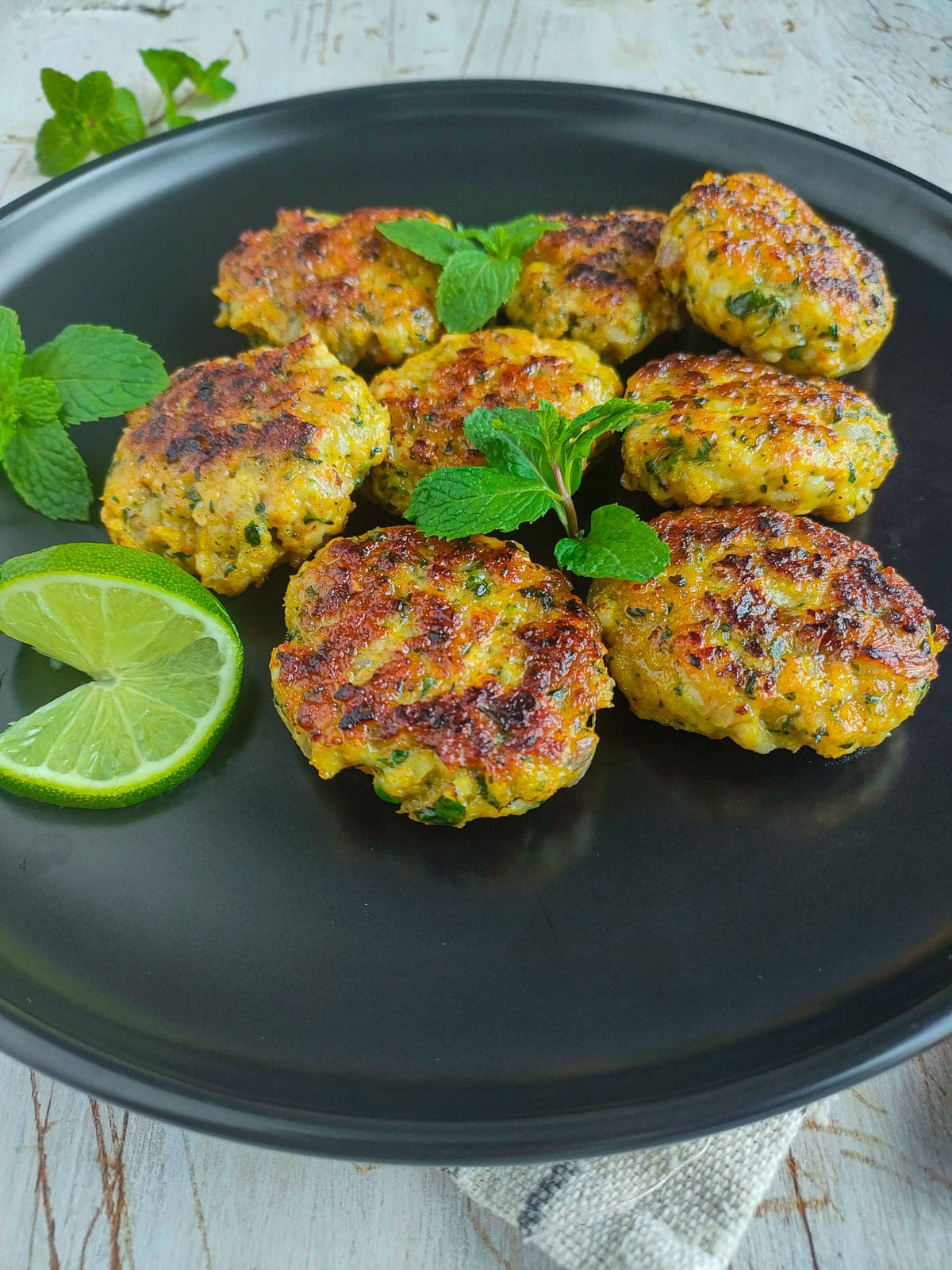 Easy Shrimp Fritters | Prawn Cutlets (no deep frying) Easy prawn fritters garnished with mint leaves and a lime slice on a black plate.