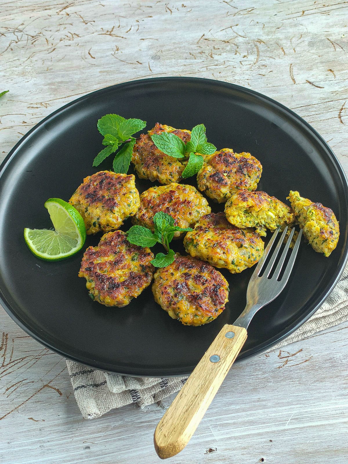 Easy Shrimp Fritters | Prawn Cutlets (no deep frying) Shrimp fritters garnished with mint leaves and a lime slice on a black plate.