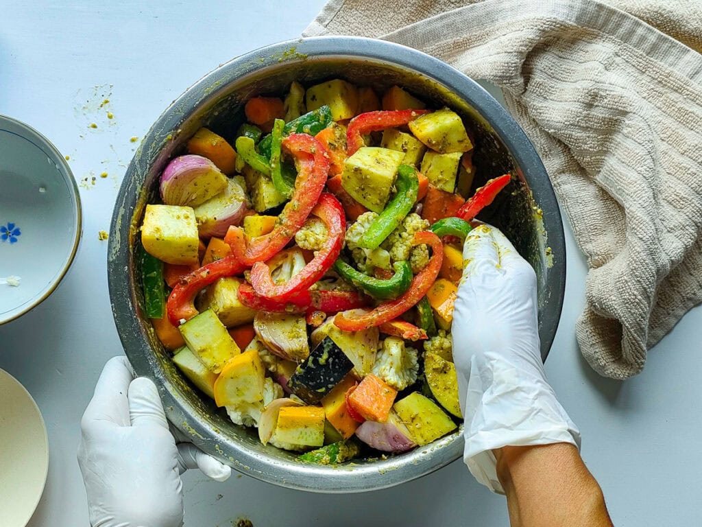Diced vegetables being tossed with pesto seasoning.