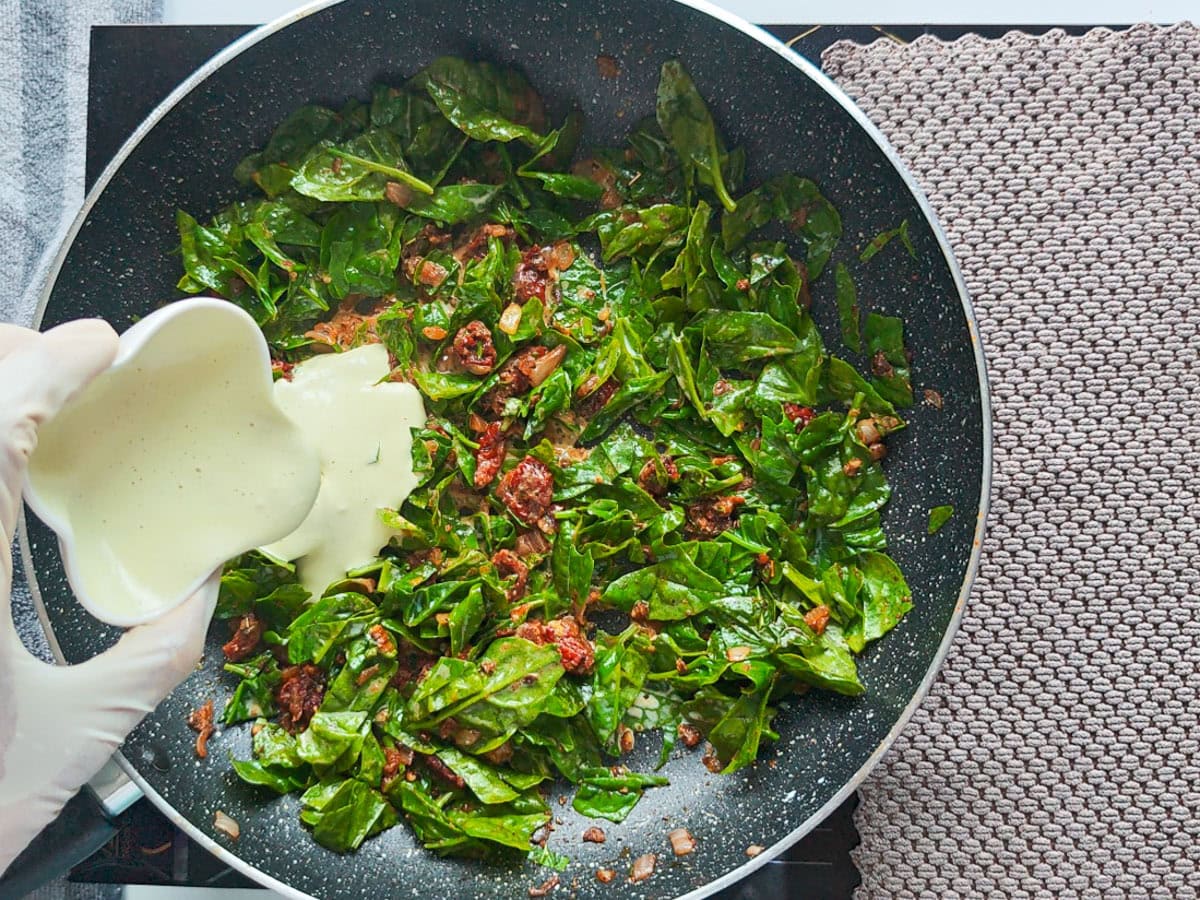 Cajun Pasta with Salmon (without cream) Cashew paste being added to tomato spinach mixture in a pan.