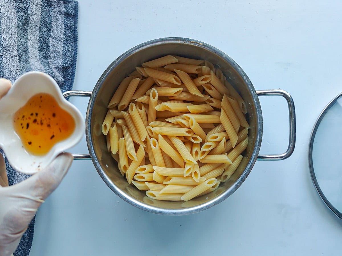 Cajun Pasta with Salmon (without cream) Oil from sun dried tomatoes being added to cooked and drained pasta in a large pot.